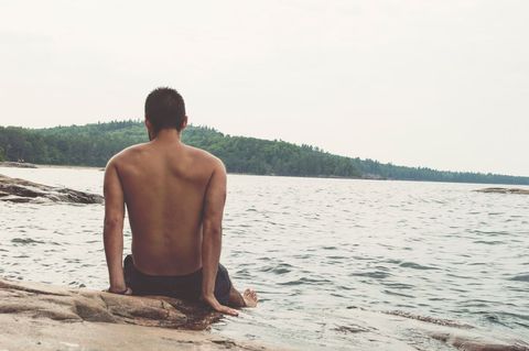 Relaxed Man Sitting on Rocky Shore Overlooking Tranquil Lake