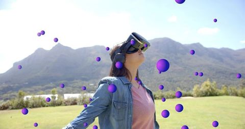 Teenage girl wearing vr headset exploring floating purple spheres in outdoor mountain meadow