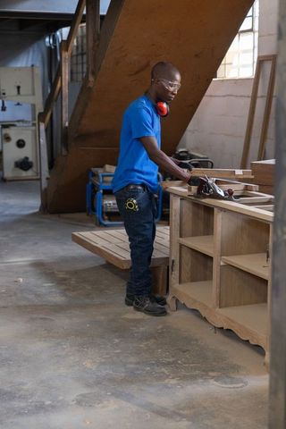 Skilled carpenter hand-planing oak cabinet on heavy workbench in industrial woodworking shop