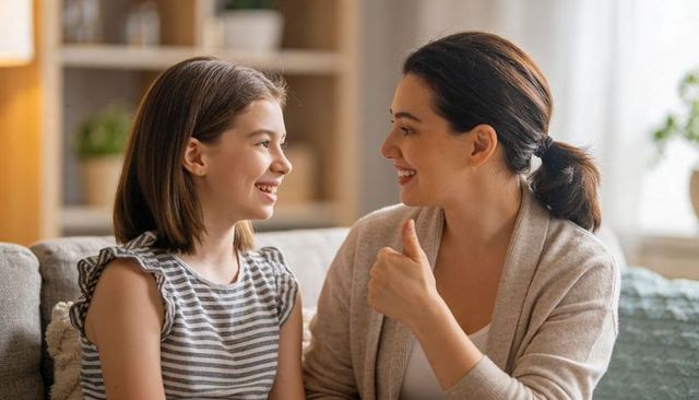 Smiling mother giving thumbs-up to daughter on cozy living room couch celebrating success