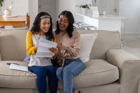 Happy Mother and Daughter Receiving Good News Letter on Sofa
