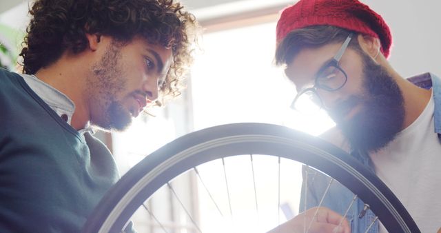 Two friends are repairing a bicycle wheel indoors. Their cooperative efforts; perfect for depicting teamwork, friendship, and DIY hobbies collaboration. It can be used for promoting bicycle maintenance services, hobby workshops, teamwork campaigns, or DIY blogs.