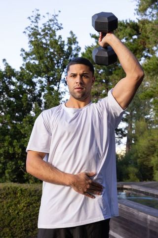 Athletic Man Lifting Dumbbell Outdoors on Pool Deck