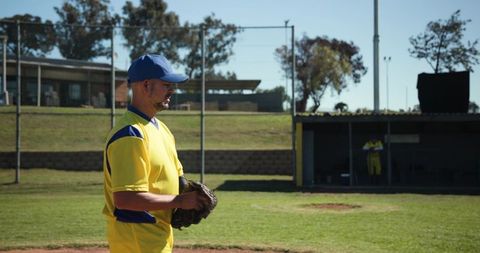 Baseball pitcher standing on mound wearing yellow uniform and blue cap on sunny field