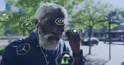 Bearded commuter adjusting wired earbud while viewing ar eco holograms in urban plaza