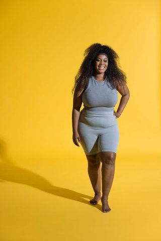 Confident african american woman walking in gray activewear on vibrant yellow backdrop