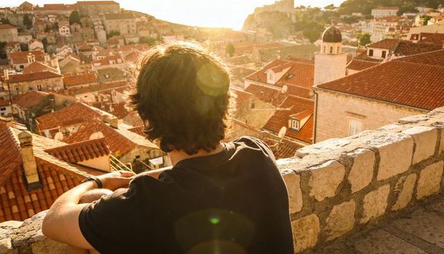 Solo traveler overlooking mediterranean coastal town from ancient stone wall at golden hour