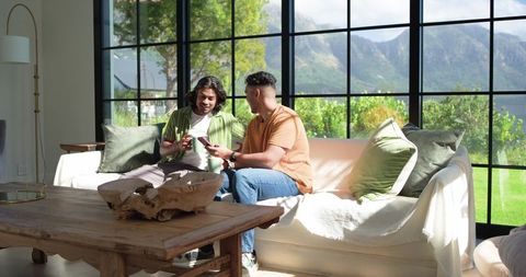 African american friends sharing coffee and smartphone on sunlit sofa with mountain view