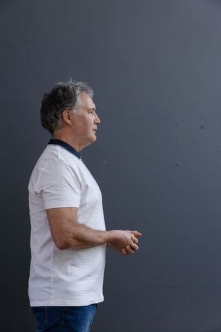 Mature Man in White Polo Contemplating Against Gray Background