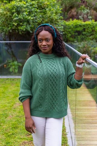African american woman in green cable knit sweater and teal headband beside glass railing