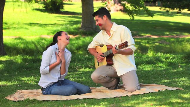 Man entertaining his laughing girlfriend with a playful guitar performance in a park. Ideal for themes of romance, outdoor dating, and carefree living. Perfect for use in promotions for dating services, music lessons, romantic getaways, and lifestyle blogs.