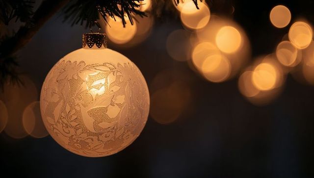 Frosted glass ornament hanging on pine branch with warm amber bokeh glow elegant holiday decor