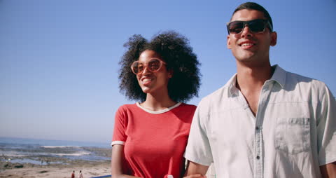 Young Couple Enjoying a Stroll by the Beach in Bright Sunlight