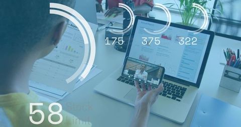 Holding phone while reviewing annual report on laptop with digital analytics overlay