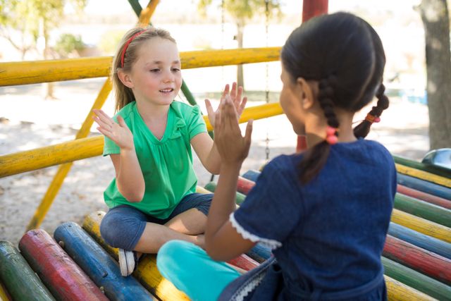 Girls playing clapping game while sitting on jungle gym at playground