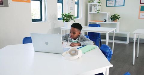 African teenage student studying with laptop and headphones in bright modern classroom