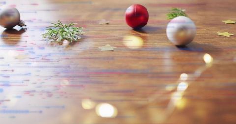 Festive red and silver baubles on wooden table with warm fairy light bokeh and evergreen