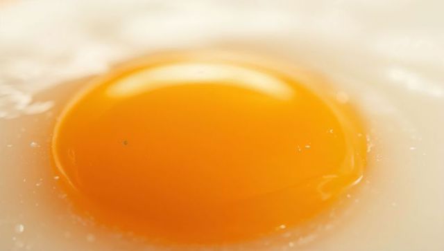 Glowing egg yolk sitting on glossy white with droplets and bubbles macro close-up