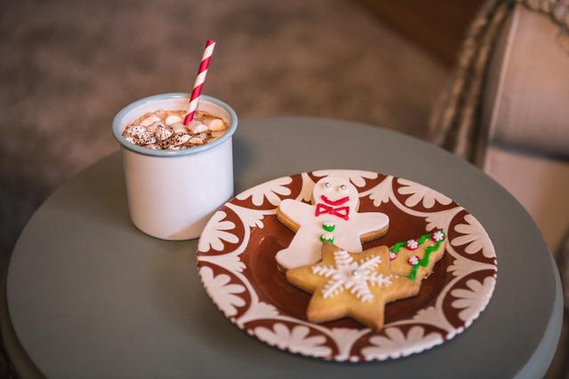 Gingerbread cookies decorated with icing and a cup of hot cocoa topped with marshmallows on a table. Perfect for holiday-themed promotions, Christmas cards, festive blog posts, or advertisements for seasonal treats.