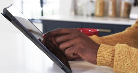 Person using tablet in cozy kitchen with red mug and mustard sweater