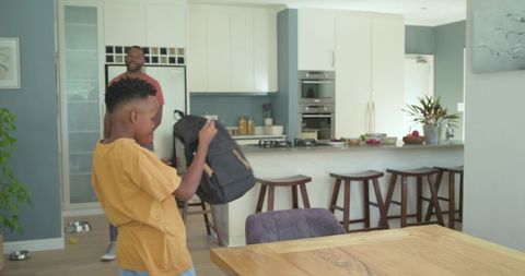 Father helping son prepare backpack for school morning in modern open-plan kitchen