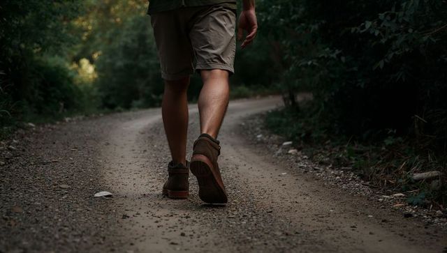 Solo hiker walking on forest dirt trail wearing khaki shorts and brown boots