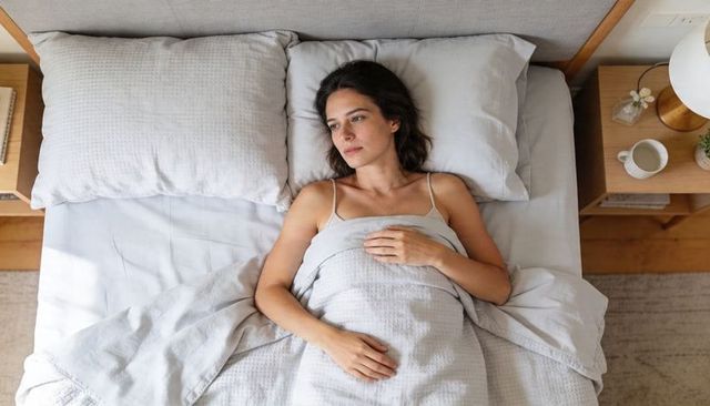 Woman lying in bed gazing contemplatively in morning light with minimalist gray bedding
