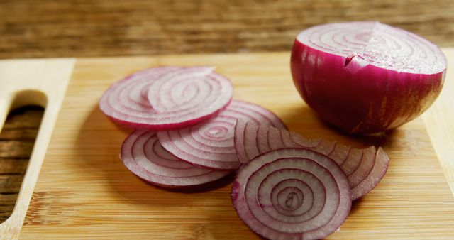 Sliced red onions are arranged on a wooden cutting board, with copy space. Their vibrant purple layers add a pop of color and hint at the flavorful addition they can make to various dishes.