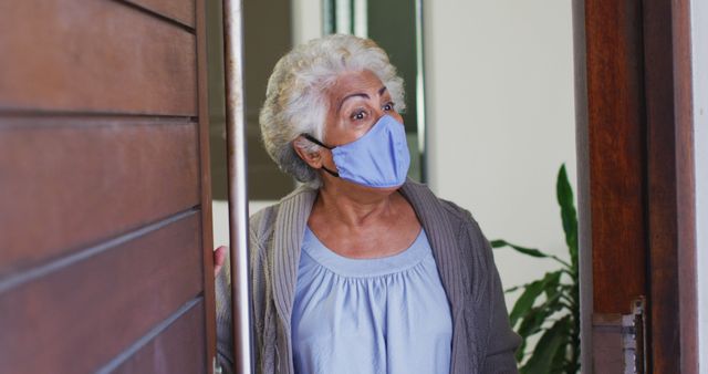African american senior woman wearing face mask opening front door and welcoming at home. retirement senior lifestyle living in quarantine lockdown concept