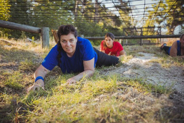 Women participating in an outdoor obstacle course, crawling under a net as part of their boot camp training. Ideal for use in articles or advertisements related to fitness, teamwork, outdoor activities, and physical challenges.