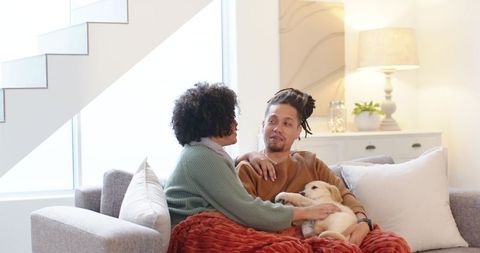 Couple cuddling on light gray sofa with puppy, cozy modern living room, warm daylight atmosphere