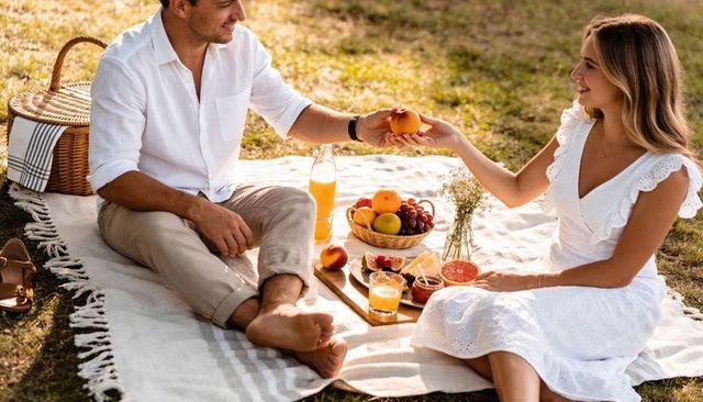Sunlit romantic picnic couple sharing fruit and juice on blanket at golden hour