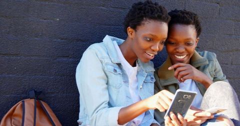 Laughing Twin Sisters Bonding and Using Smartphone Outdoors