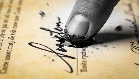 Pressing inked fingertip spreading black ink blot over parchment signature and calligraphy