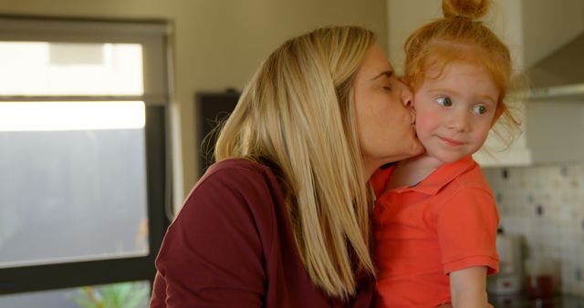 A Caucasian woman is affectionately kissing a young girl on the cheek, with copy space. Their warm interaction suggests a loving family moment in a cozy home setting.