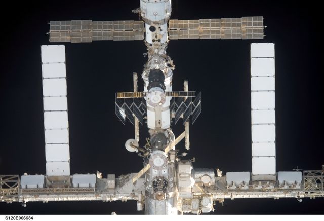 Image captures a segment of the International Space Station with the Space Shuttle Discovery approaching for docking. Useful for educational content, technology presentations, aerospace company materials, and science exhibitions. The image highlights the complexity and advanced engineering of space structures, emphasizing international collaboration and space exploration milestones.
