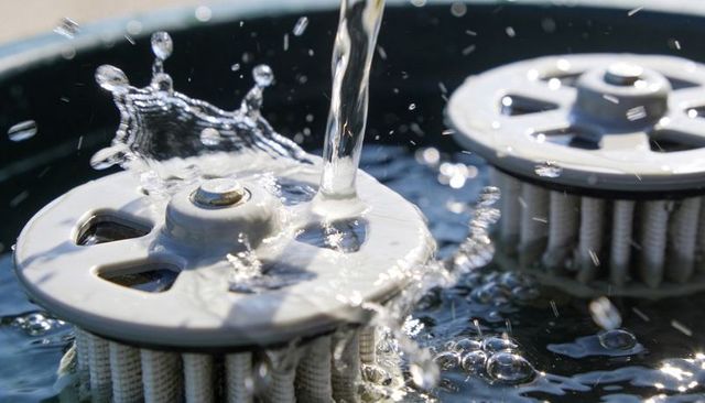 Close-up water splashing over pleated filter cartridges creating droplets ripples and bokeh