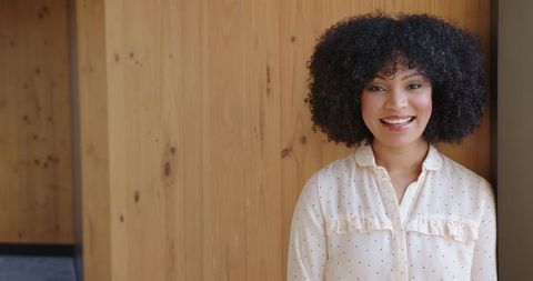 Smiling woman in polka dot blouse leaning against wood paneled wall