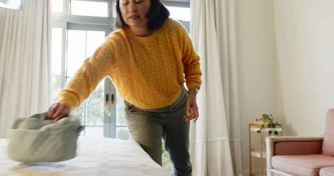 Woman Arranging Laundry Basket on Bed in Bright Bedroom