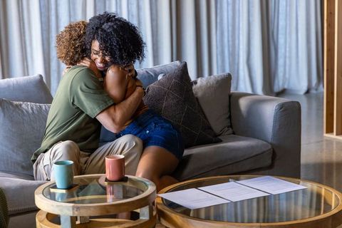 Interracial couple embracing on cozy living room sofa, sharing hug after signing papers