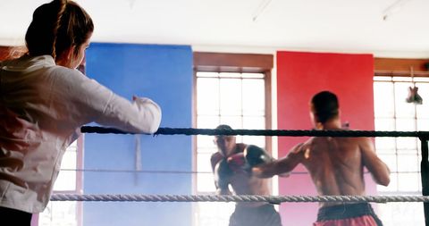 Boxing coach watching male athletes training in ring