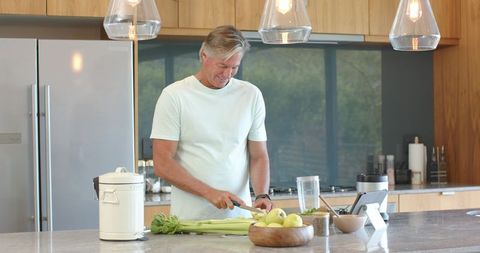 Senior man chopping vegetables while following recipe on tablet at modern kitchen island