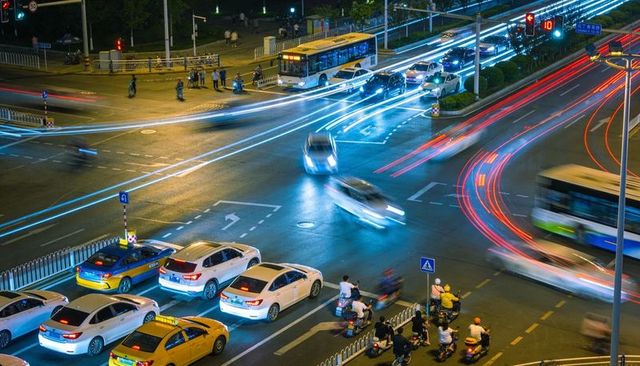 Night city intersection with neon light trails long exposure traffic, taxis and scooters