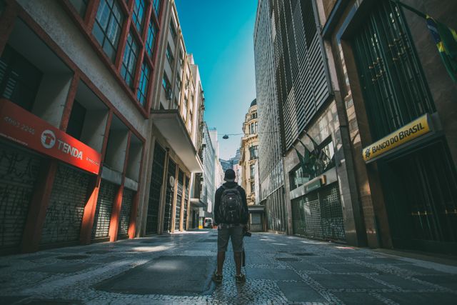 This image depicts a lone backpacker standing in the middle of an empty urban street, surrounded by tall buildings in downtown. The photo represents themes of travel, exploration, and solitude. Ideal for use in travel blogs, tourism advertisements, architectural websites, or urban adventure promotions.