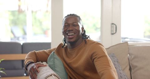 Joyful african american man laughing on couch in cozy living room