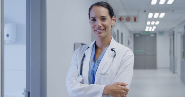 Confident young Caucasian woman doctor stands in a hospital corridor. Her professional demeanor conveys trust and competence in the healthcare setting.