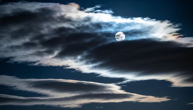 Full Moon Peeking Through Silvery Cloud Bands Over Night Sky With Moonlight Glow and Faint Stars