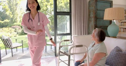 Nurse assisting elderly woman with walker in light-filled living room