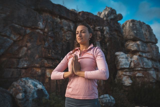 Caucasian woman with joined hands meditating while standing in the mountains. adventure, lifestyle and travel concept