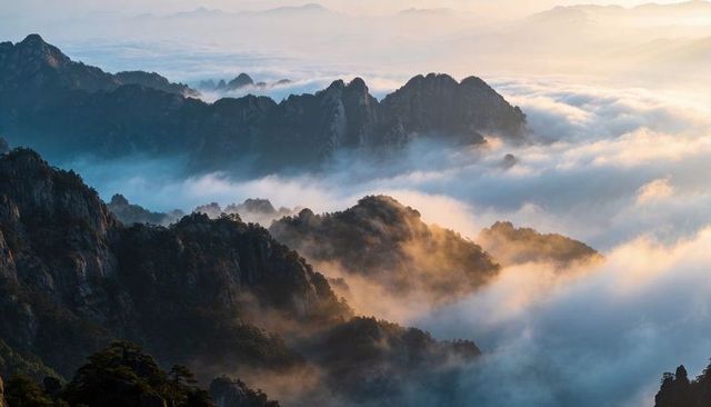 Sunlit jagged peaks rising above sea of clouds at dawn, misty mountain ridge